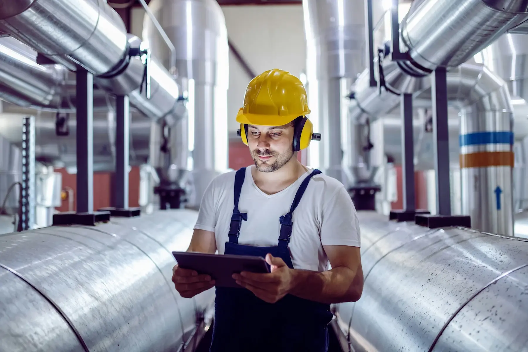 Técnico consultando una tablet entre tuberías industriales